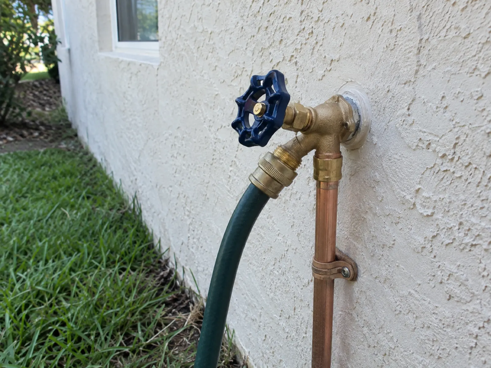 New brass outdoor hose bib installed on a stucco wall